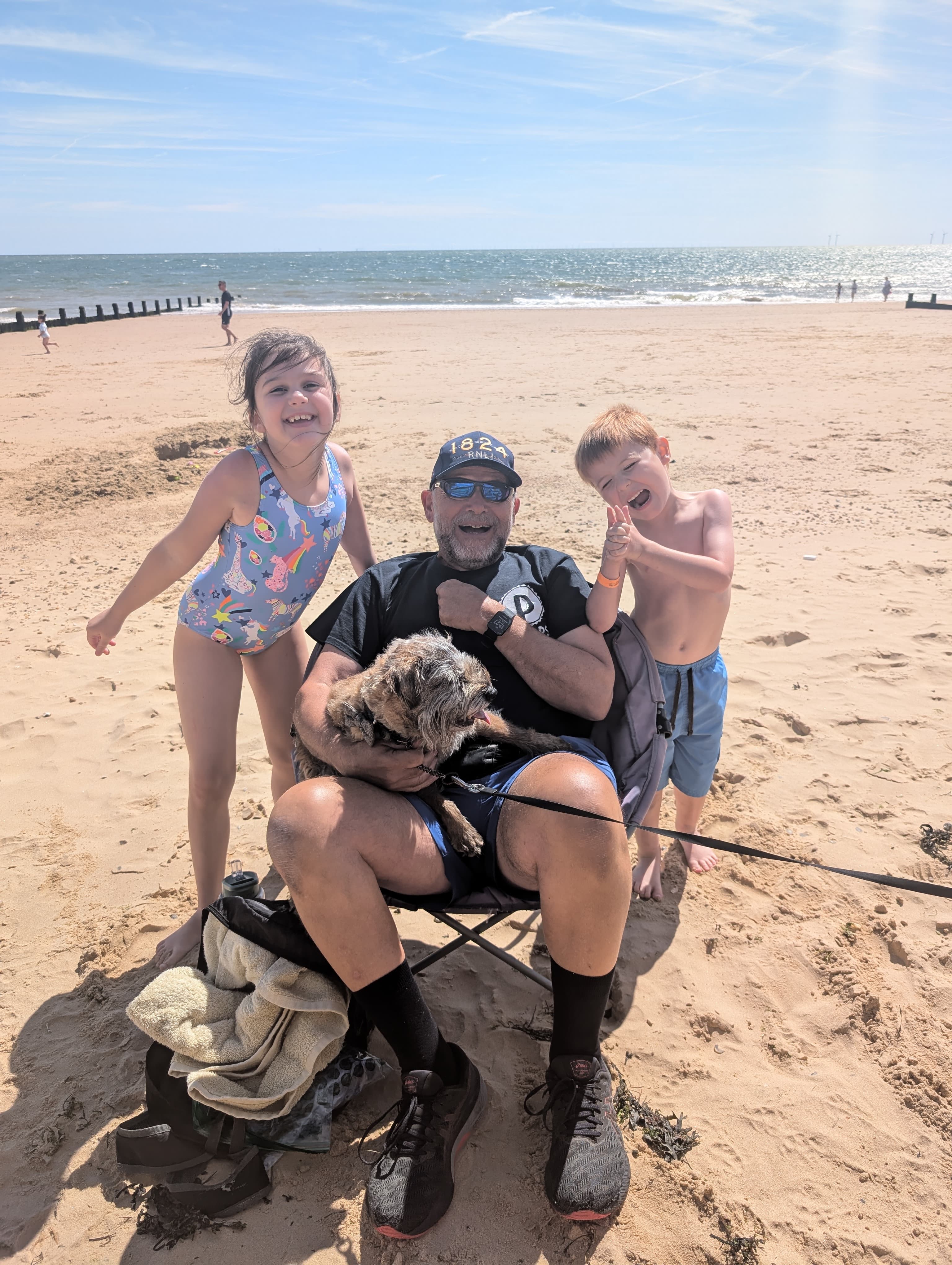A grandfather on the beach with his two young grandchildren and the family dog
